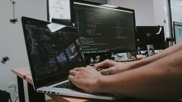 複数の画面にコードを表示しながらノートパソコンで作業する様子